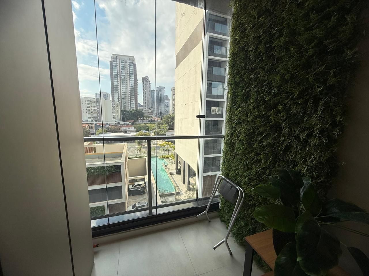 A balcony with a view of a cityscape, a green wall, and a chair.