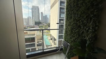A balcony with a view of a cityscape, a green wall, and a chair.