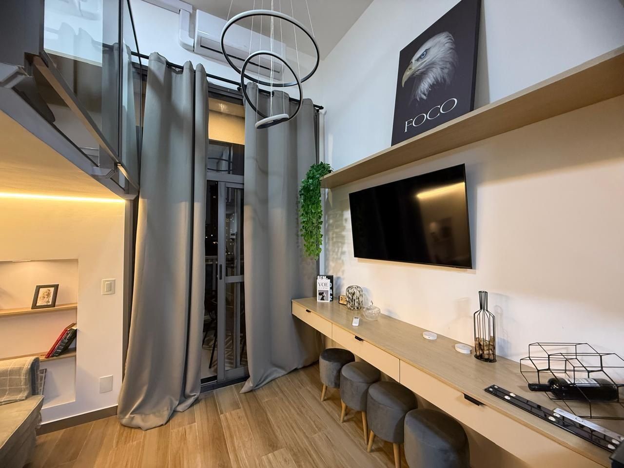 A modern kitchen with a built-in stove, a flat-screen TV mounted above the counter, and a sliding glass door leading to a balcony.