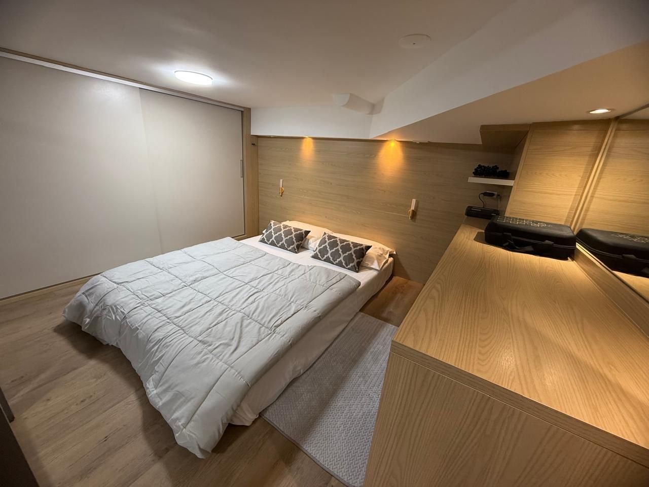 A modern bedroom with a bed, wooden headboard, and built-in storage.