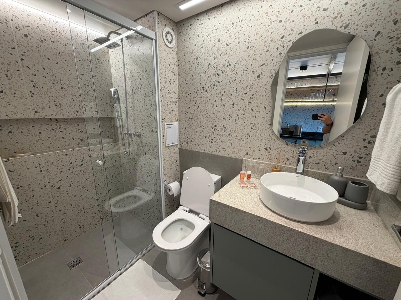 A modern bathroom with a glass-enclosed shower, a white toilet, and a sink with a mirror above it.