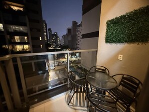 Een balkon met glazen hekwerk, een ronde tafel en vier stoelen.