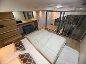 Een slaapkamer met een bed, een bureau, een stoel, een spiegel en een glazen schuifdeur die leidt naar een balkon.