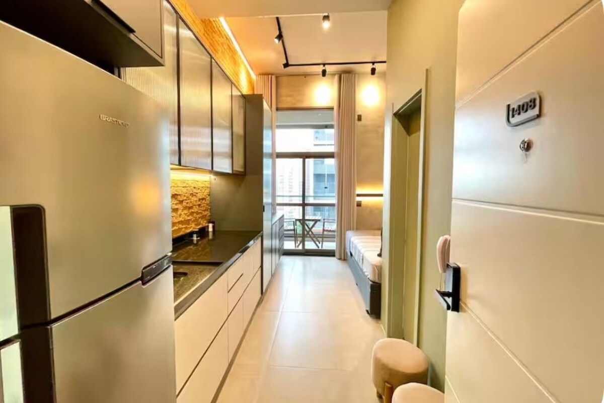 Un couloir étroit, avec une kitchenette sur la gauche, un lit sur la droite et une fenêtre au fond.