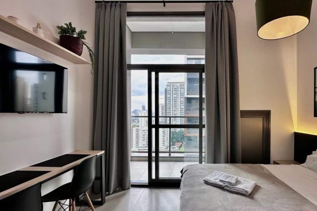 Une chambre d’hôtel moderne équipée d’un lit, d’un bureau, d’une télévision et d’une grande fenêtre avec des rideaux.