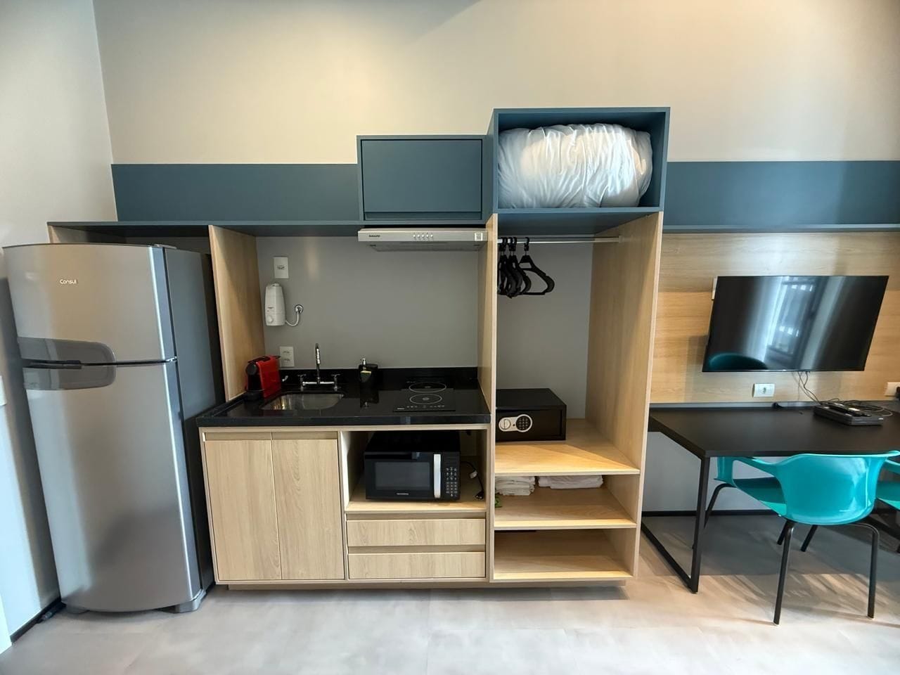 Uma cozinha compacta equipada com geladeira, micro-ondas, fogão e uma TV de tela plana.