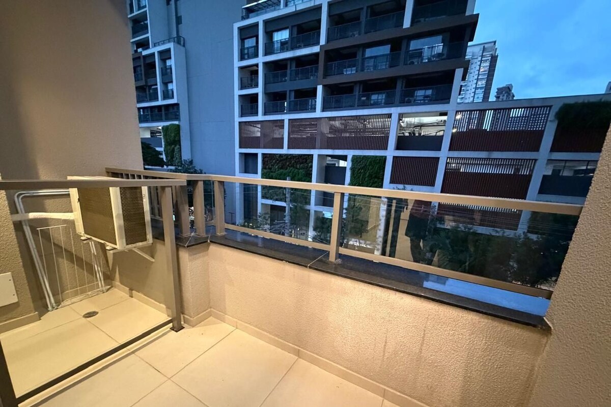 Un balcon doté d’une balustrade en verre, offrant une vue sur un immeuble moderne, et un sol carrelé.
