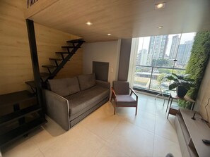 Ein stilvolles Wohnzimmer mit Sofa, Sessel, Treppe und Blick auf hohe Gebäude durch große Fenster.
