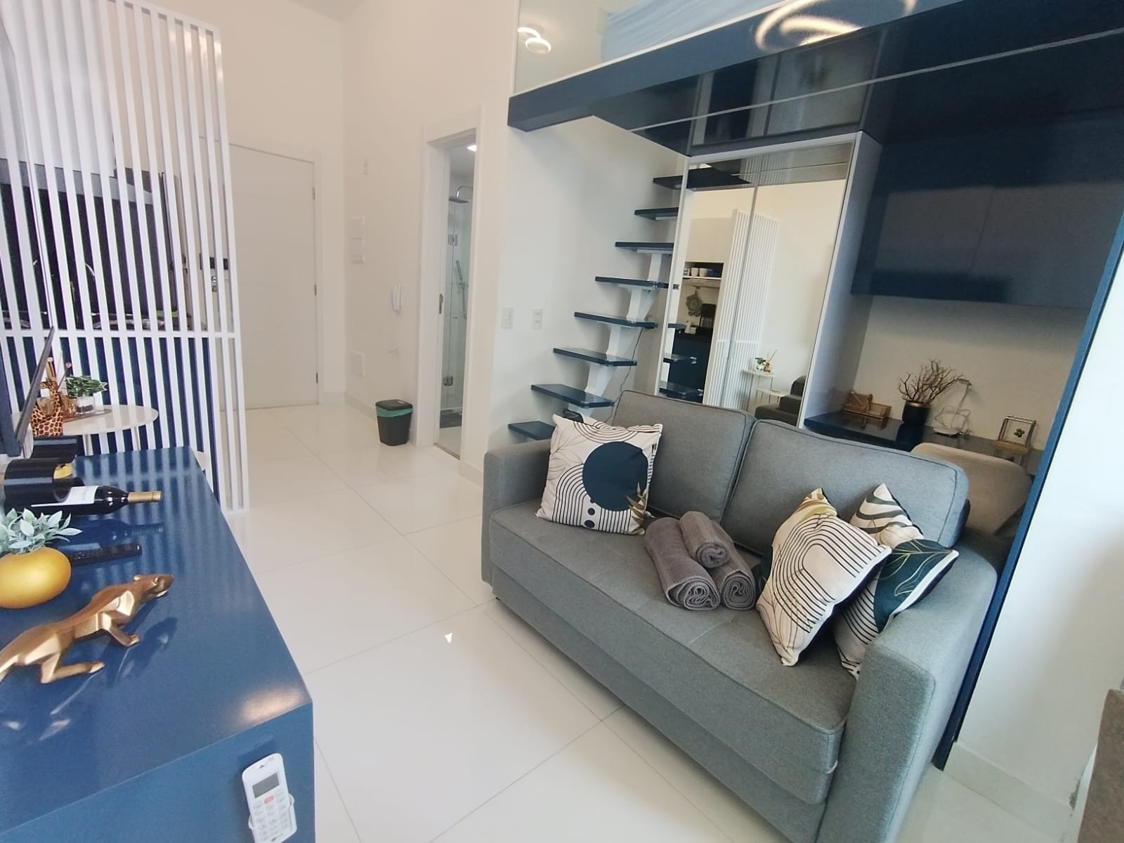 Uma sala de estar moderna com um sofá cinzento, uma mesa de centro azul e uma escada com guarda de cor preta.