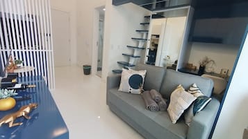 Uma sala de estar moderna com um sofá cinzento, uma mesa de centro azul e uma escada com guarda de cor preta.