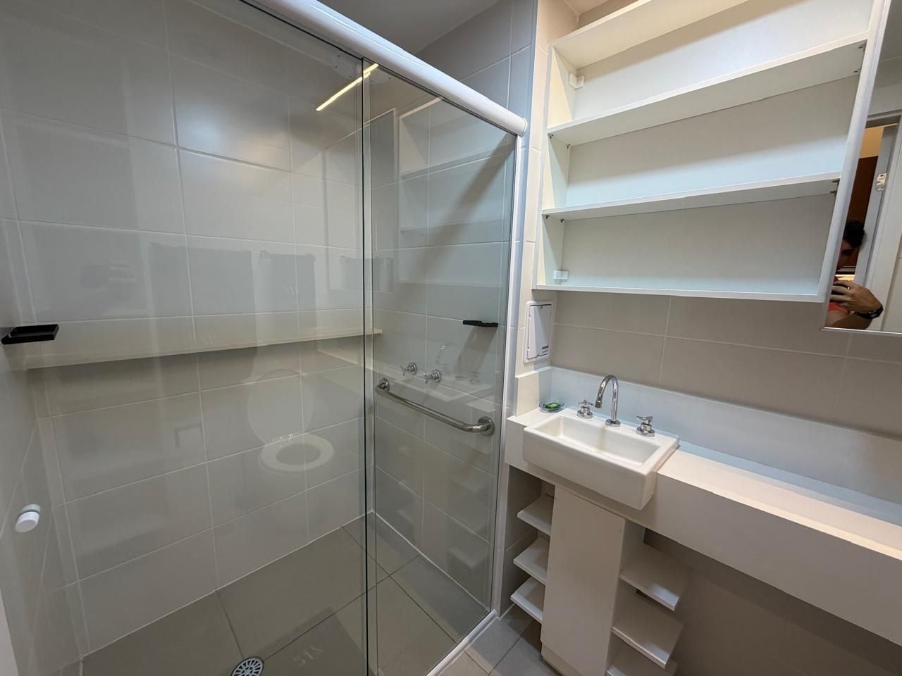 Un baño moderno con cabina de ducha de vidrio, un lavabo blanco y estantes empotrados.