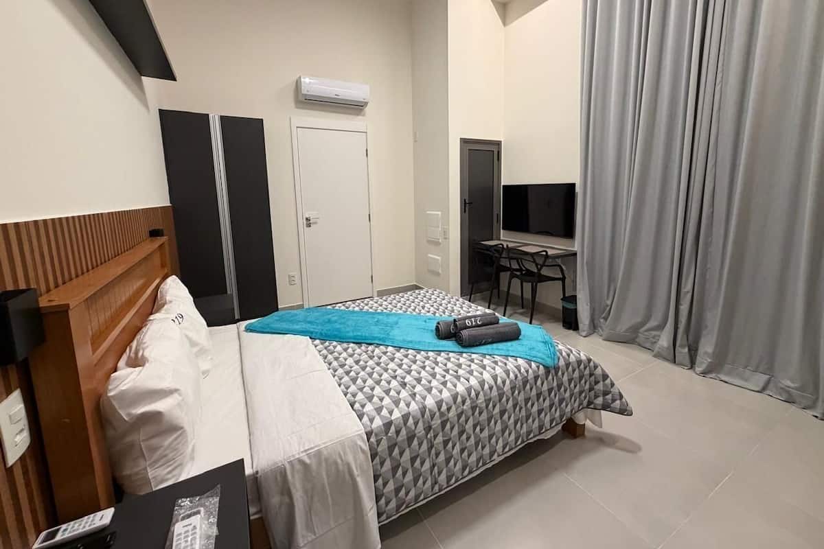 Une chambre d’hôtel avec un lit, un bureau, une télévision et une fenêtre avec des rideaux.