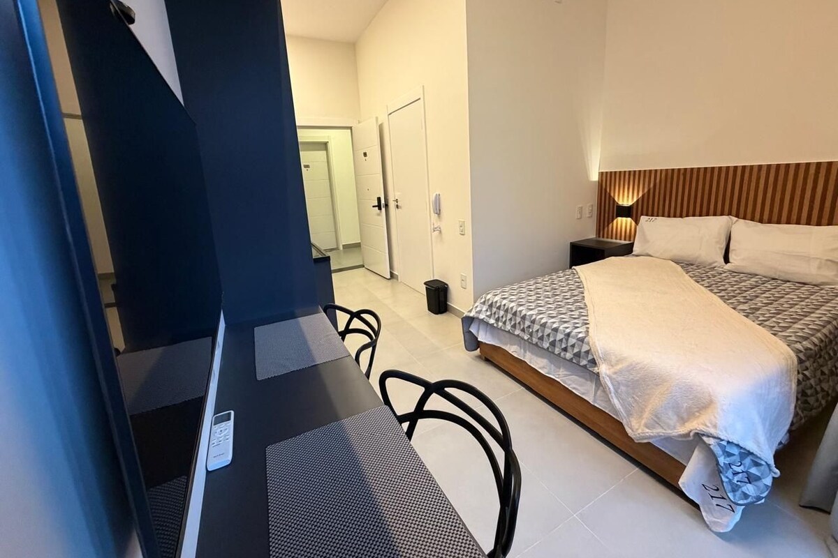 Een hotelkamer met een bed, nachtkastje, stoel en uitzicht op de gang.
