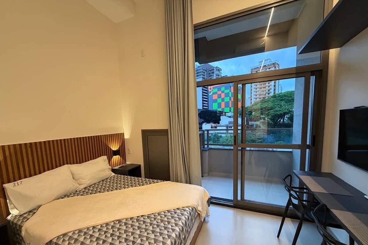 Une chambre d’hôtel moderne dotée d’un grand lit, d’un bureau et d’un balcon offrant une vue sur la ville.