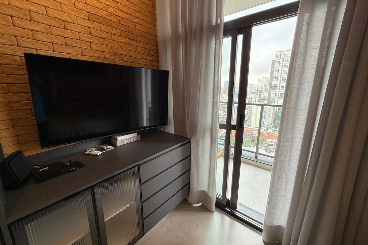 A modern living room with a flat-screen TV, a built-in sound system, and a view of a cityscape through a large window.