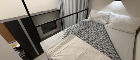 A single bed with a geometric-patterned mattress and white bedding, a black metal headboard, and a window with curtains.