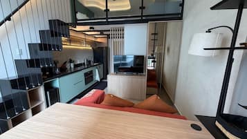 A modern kitchen with a dining area, a staircase, and a small seating area with cushions.