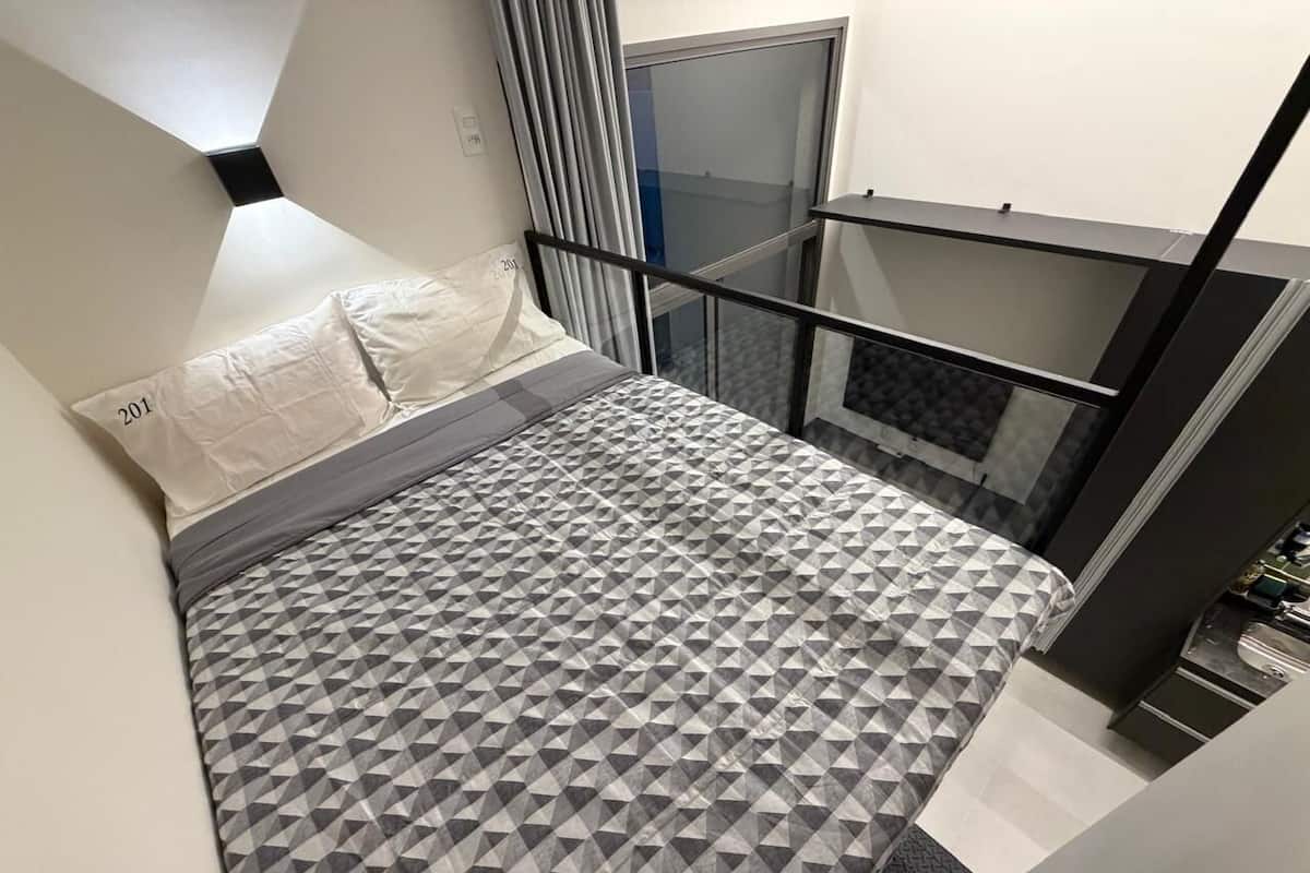 Une chambre à coucher avec une couvre-lit à motifs géométriques, un oreiller blanc et une balustrade en verre.