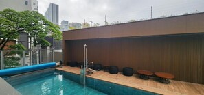 Un área de piscina en la azotea con terraza de madera, mobiliario y vistas al horizonte de la ciudad.