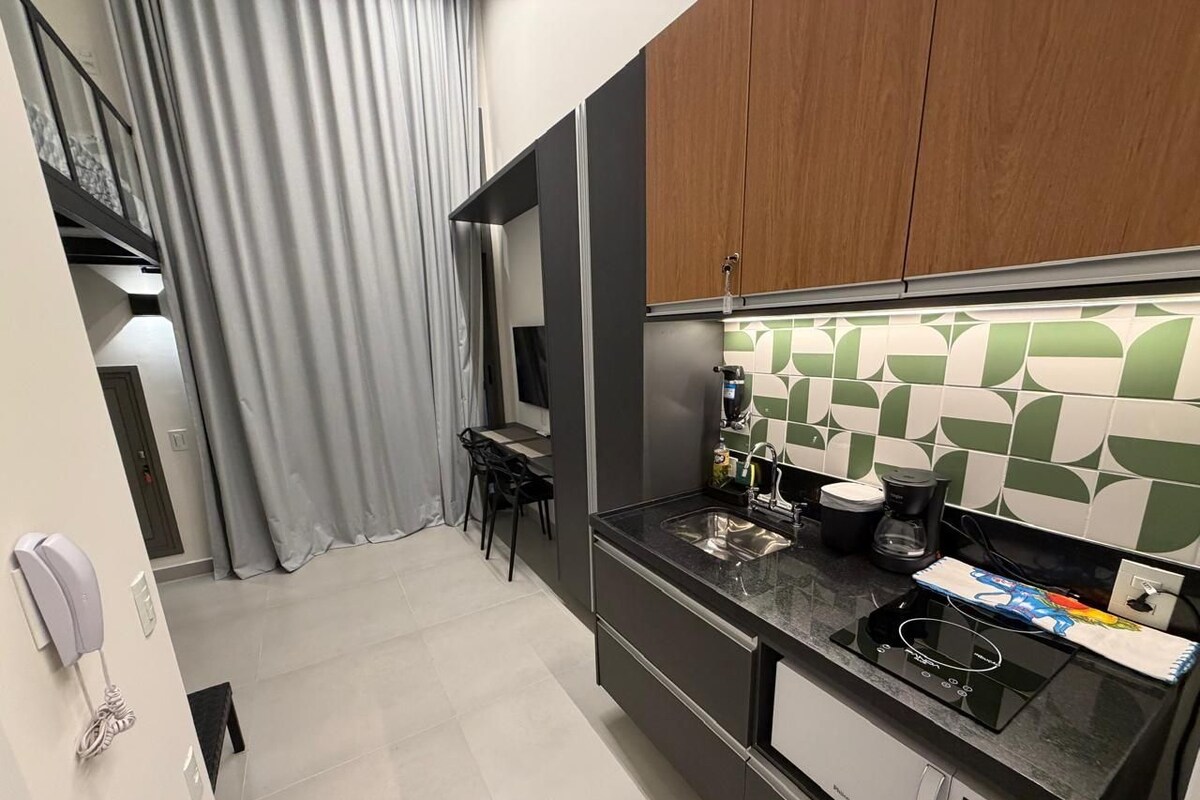 A compact kitchen with a modern design, featuring a black countertop, a coffee maker, and a built-in oven.