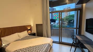 A modern hotel room with a large bed, a desk, and a balcony with a city view.
