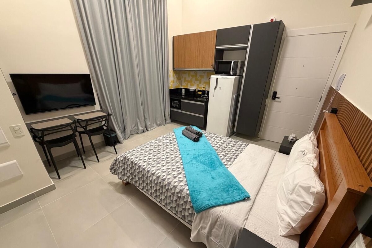 Een slaapkamer met een bed, televisie, bureau en kitchenette.