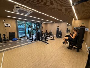 A gym with exercise equipment, a bench, and a person using a phone. - Haus Mitre 370 (São Paulo)