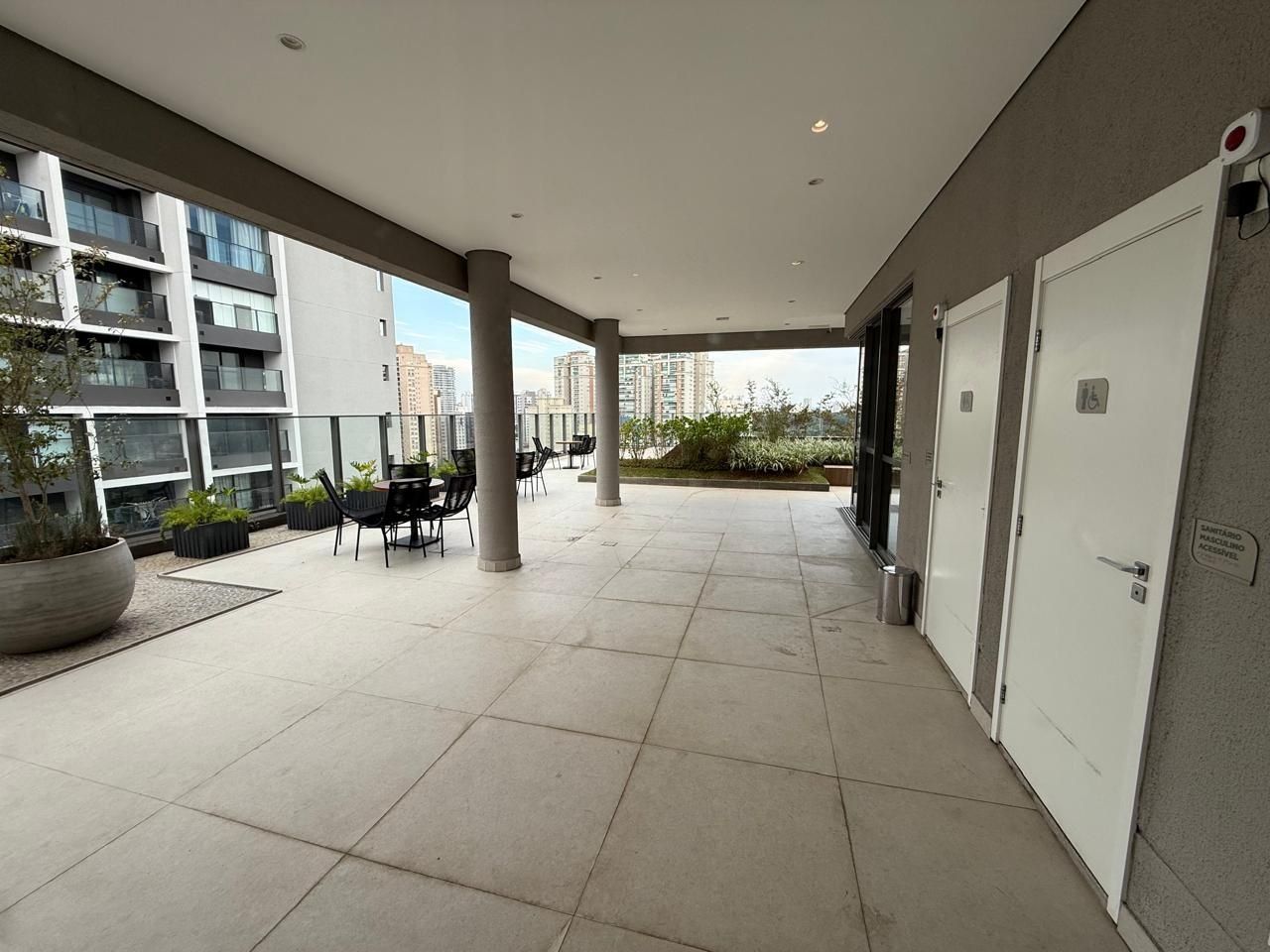 Uma área externa coberta com piso de azulejos, assentos e vista para edifícios altos.