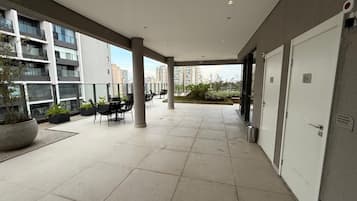 Uma área externa coberta com piso de azulejos, assentos e vista para edifícios altos.
