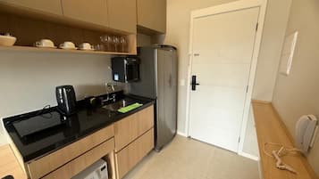 A compact kitchen with a black countertop, stainless steel refrigerator, and wooden cabinets.