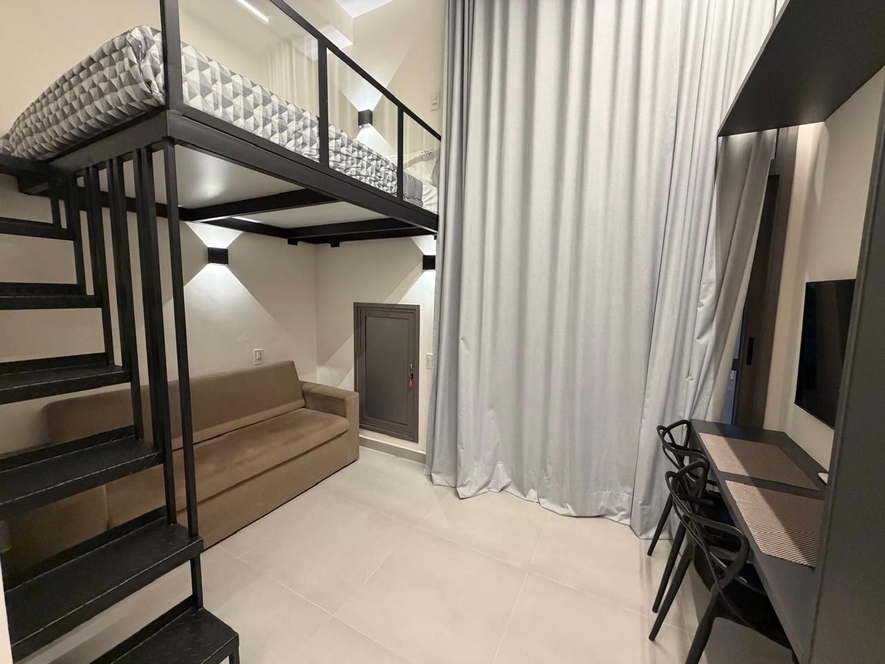 A modern interior with a bunk bed, a sofa, a desk with chairs, and a curtain.