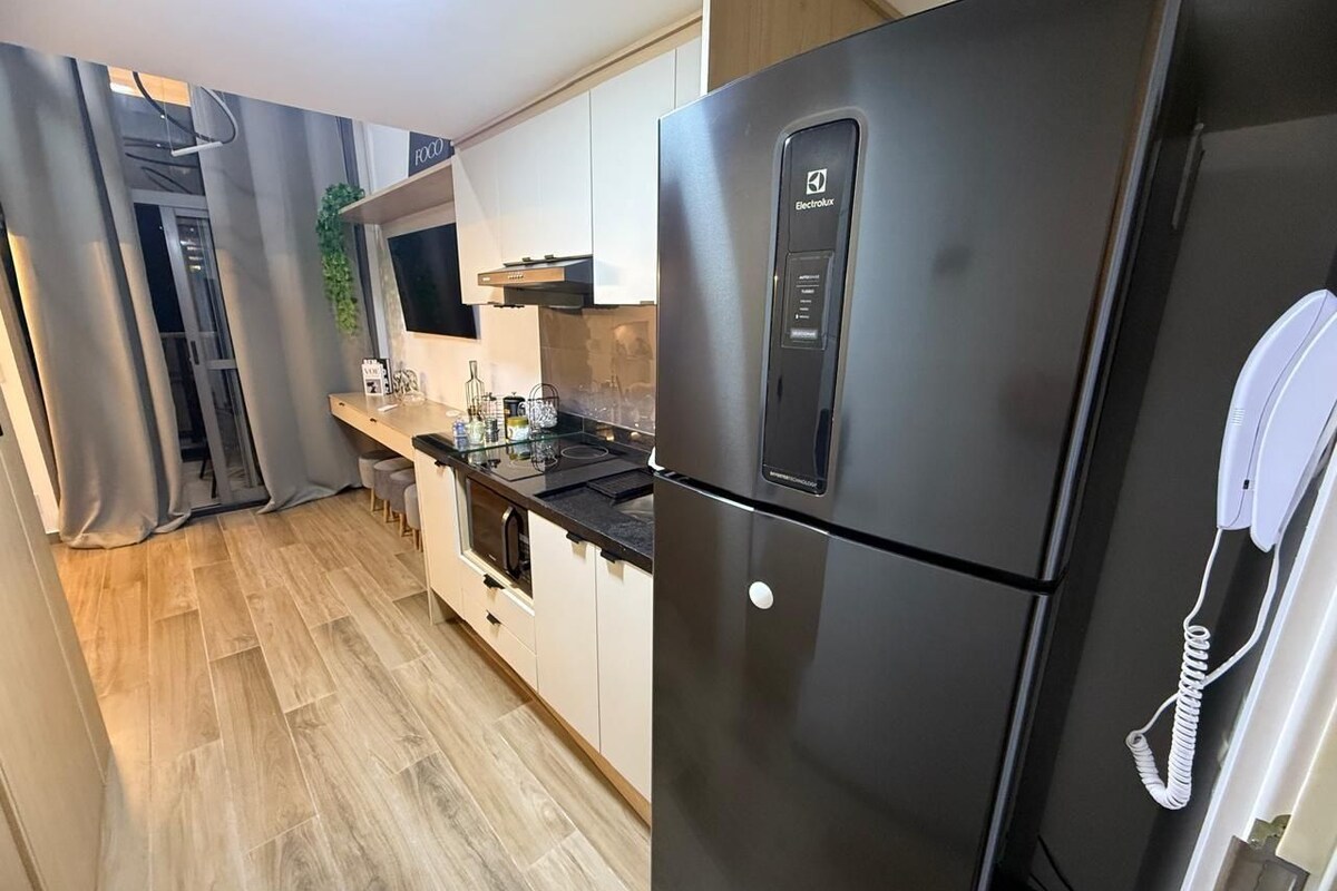 A modern kitchen with a stainless steel refrigerator, a built-in oven, and a small dining area.
