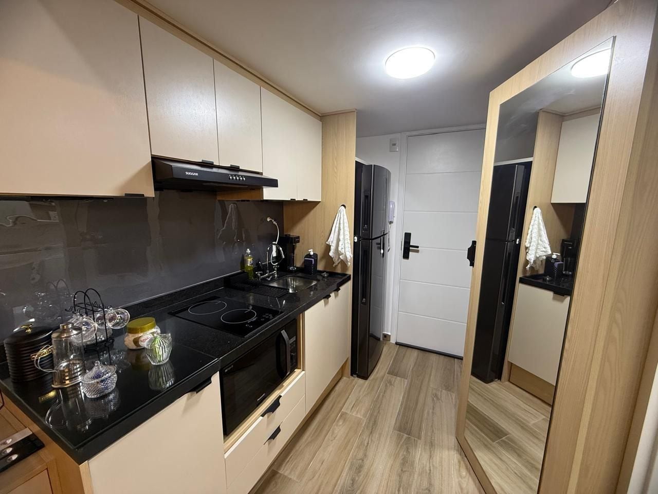 A compact kitchen with a black countertop, stainless steel appliances, and light wood flooring.