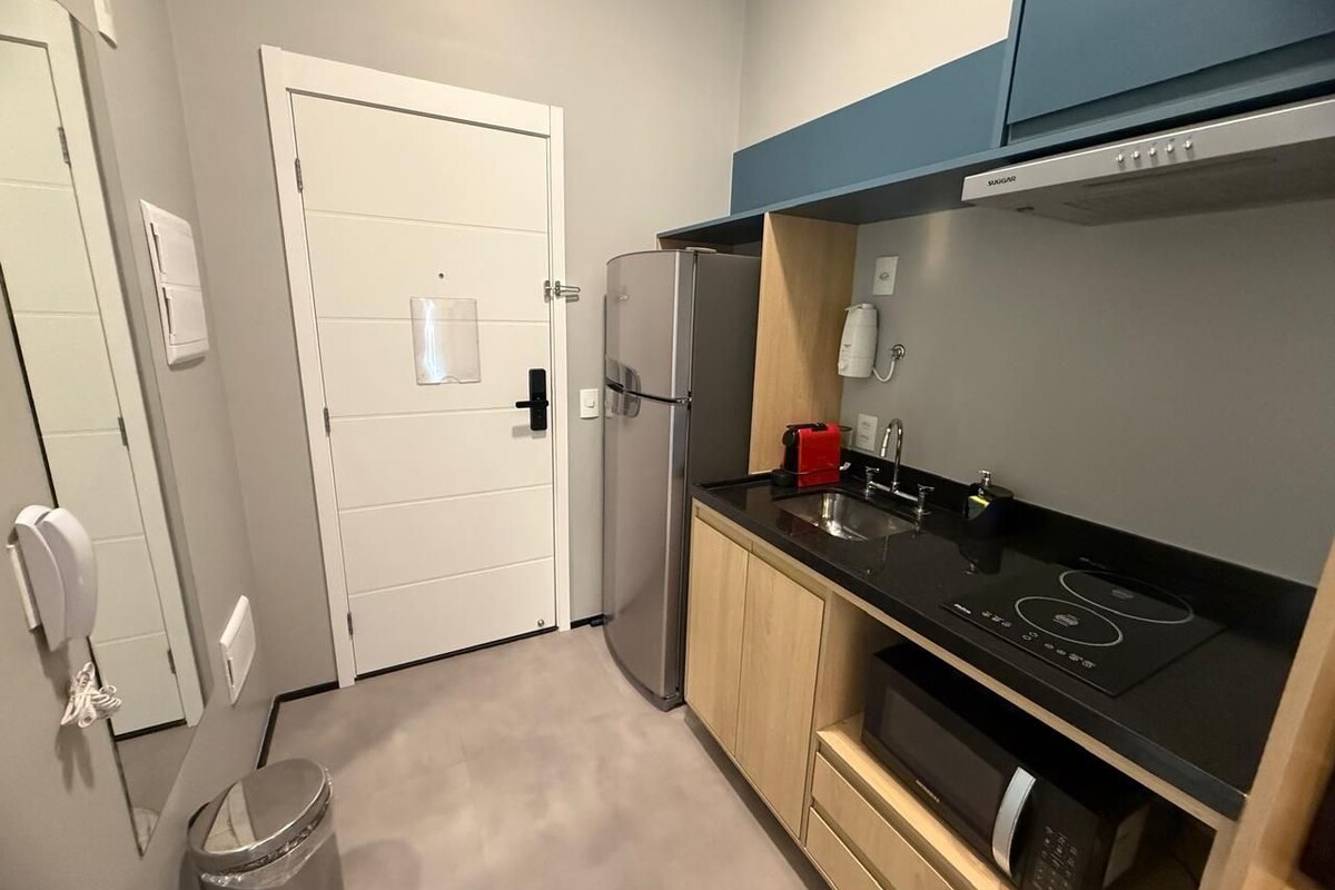 Een kleine keuken met een koelkast, een fornuis en houten kastjes.
