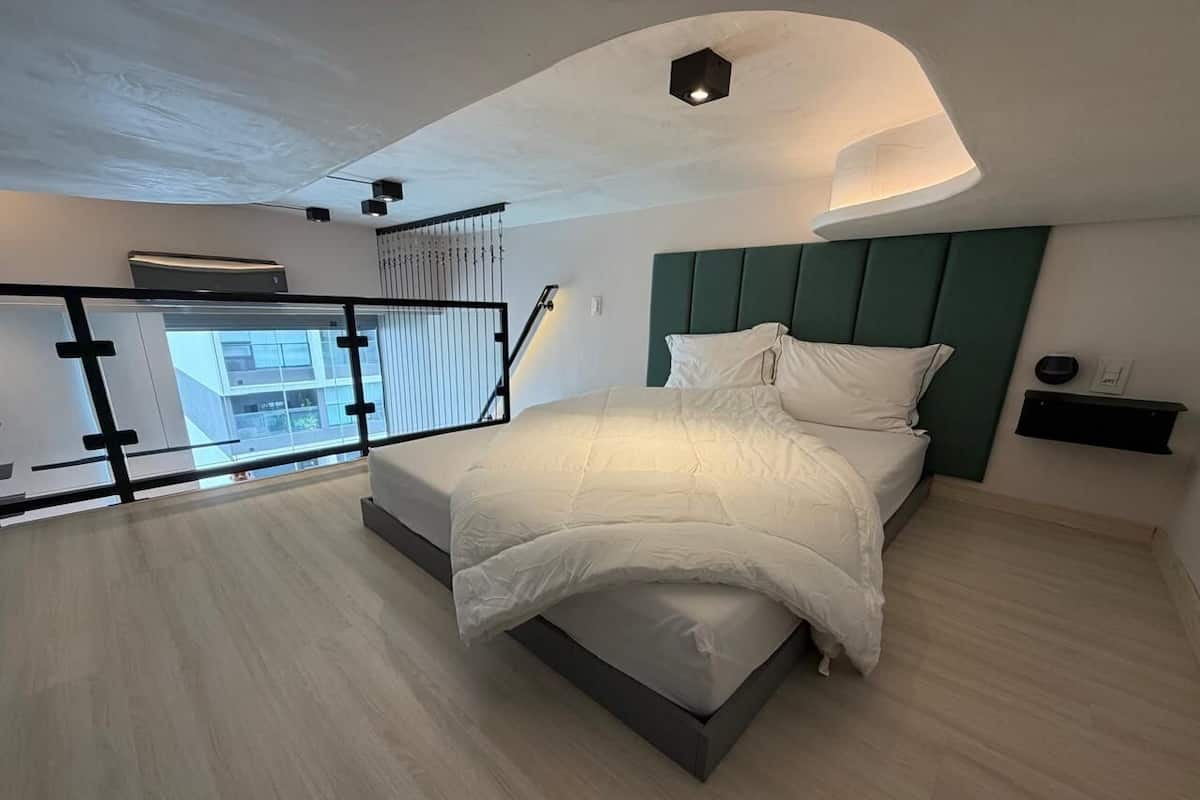 Une chambre moderne avec un lit, une table de chevet, une étagère fixée au mur et un balcon doté d’une balustrade.
