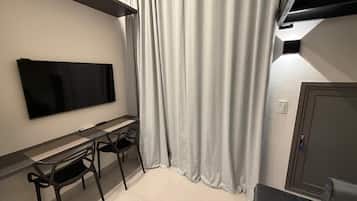 A modern room with a flat-screen TV mounted on the wall, a desk with two chairs, and a large window with curtains.