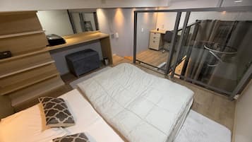 Quarto com cama, escrivaninha, cadeira, espelho e porta de vidro corrediça que dá para uma varanda.