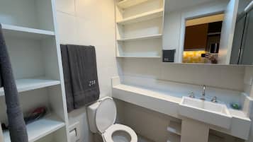 A bathroom with a toilet, a sink, and a mirror. There are shelves and a towel rack.
