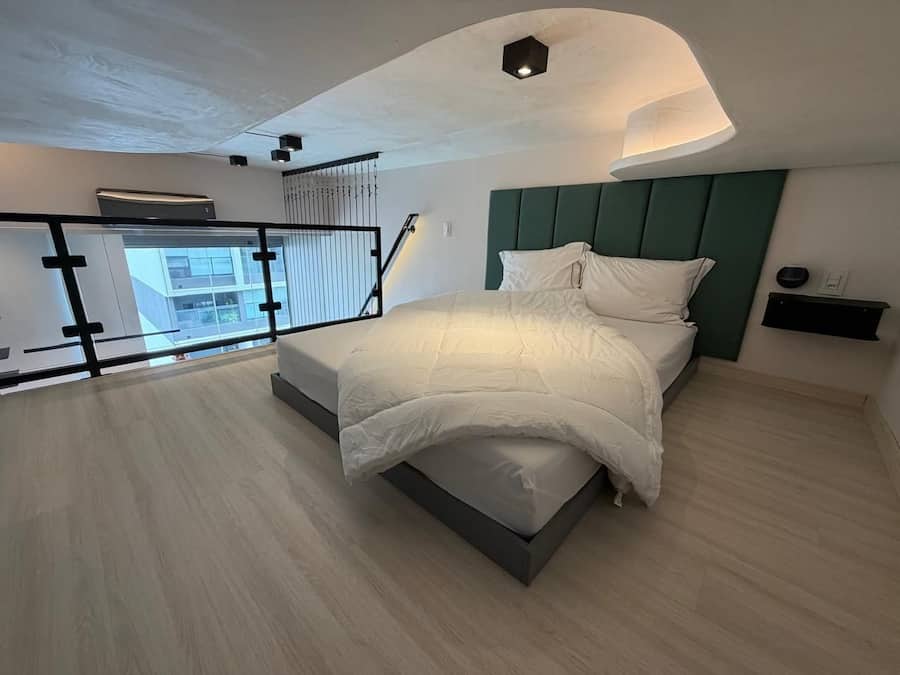 A modern bedroom with a bed, a nightstand, a wall-mounted shelf, and a balcony with a railing.