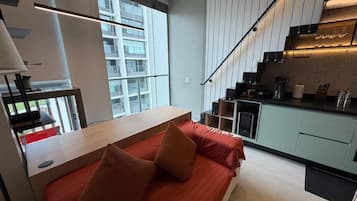 A modern loft bedroom with a large window, a kitchen area, and a staircase.