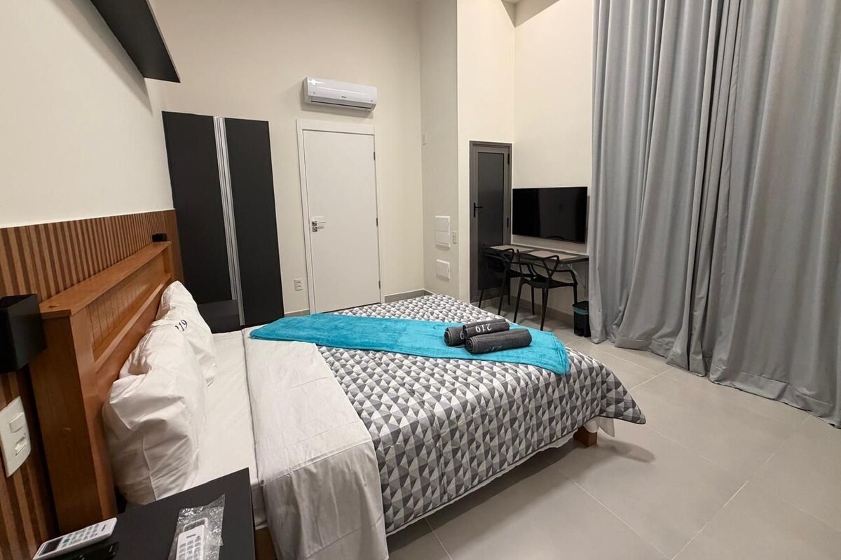 Een hotelkamer met een bed, bureau, televisie en een raam met gordijnen.