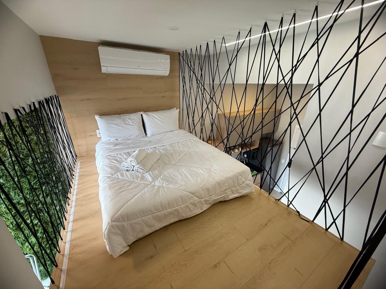 Una camera da letto con un letto, pavimento in legno, parete bianca e un divisorio in metallo nero.