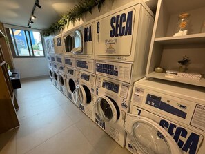Un cuarto de lavandería con varias lavadoras, cada una etiquetada con 'SECA' y 'LAVANDERÍA'.