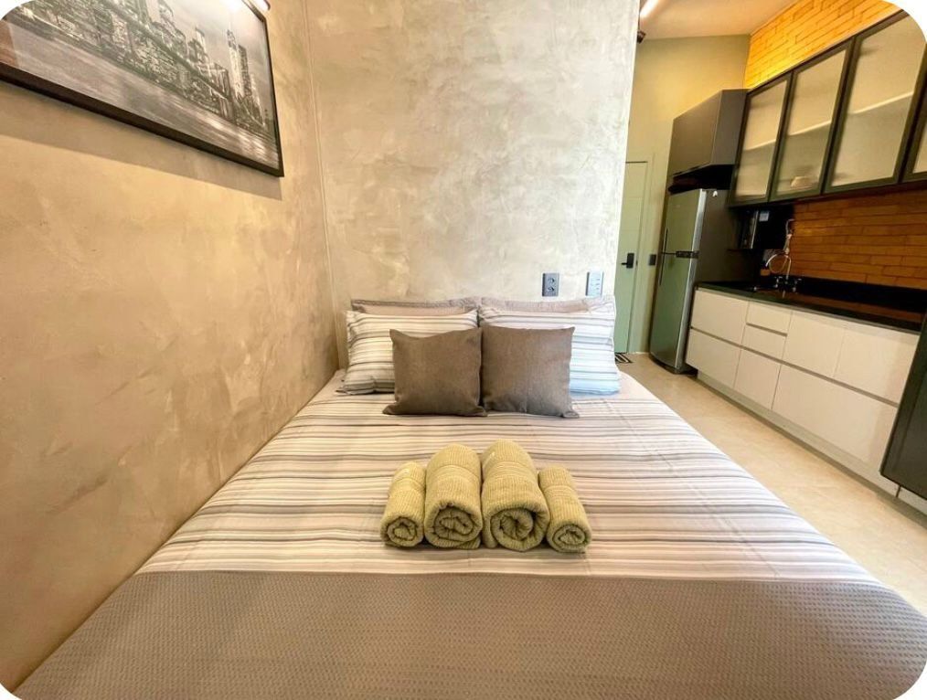 A hotel room with a bed, pillows, a kitchen area, and a framed picture on the wall.