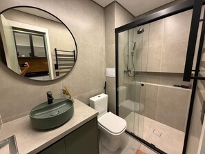 Een moderne badkamer met een ronde spiegel, een wastafel, een toilet en een douchecabine met glazen wanden.