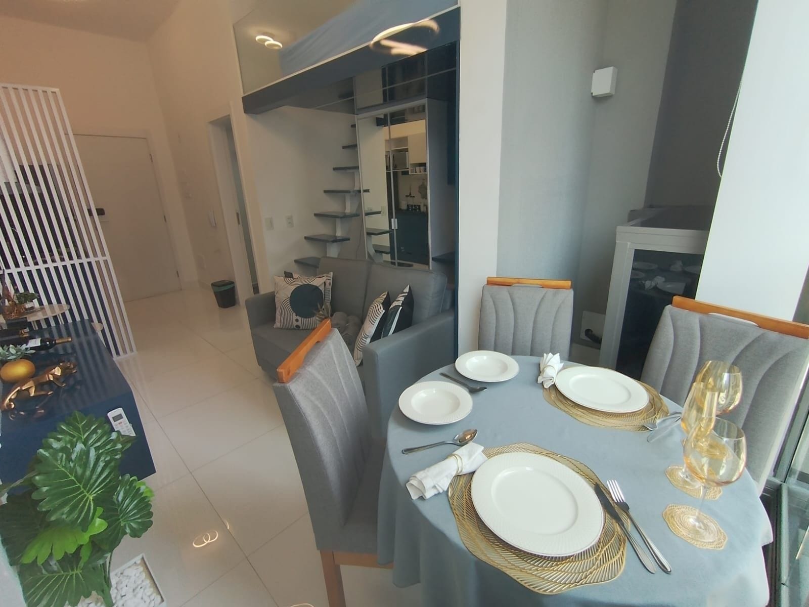 En spiseplads med et bord dækket til fire personer, inklusive tallerkener, bestik og et vinglas.