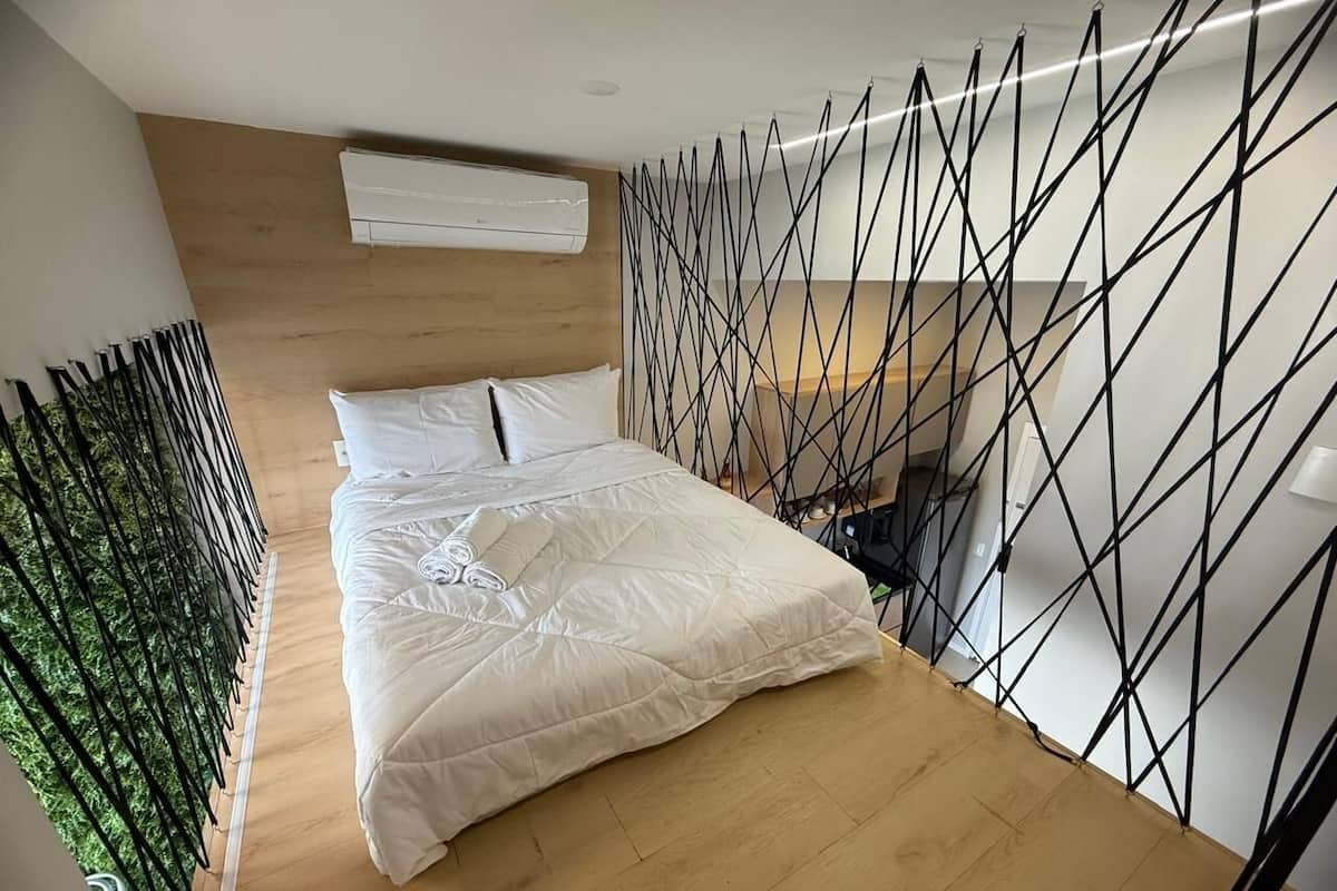 Une chambre à coucher avec un lit, un plancher en bois, un mur blanc et une cloison en métal noir.