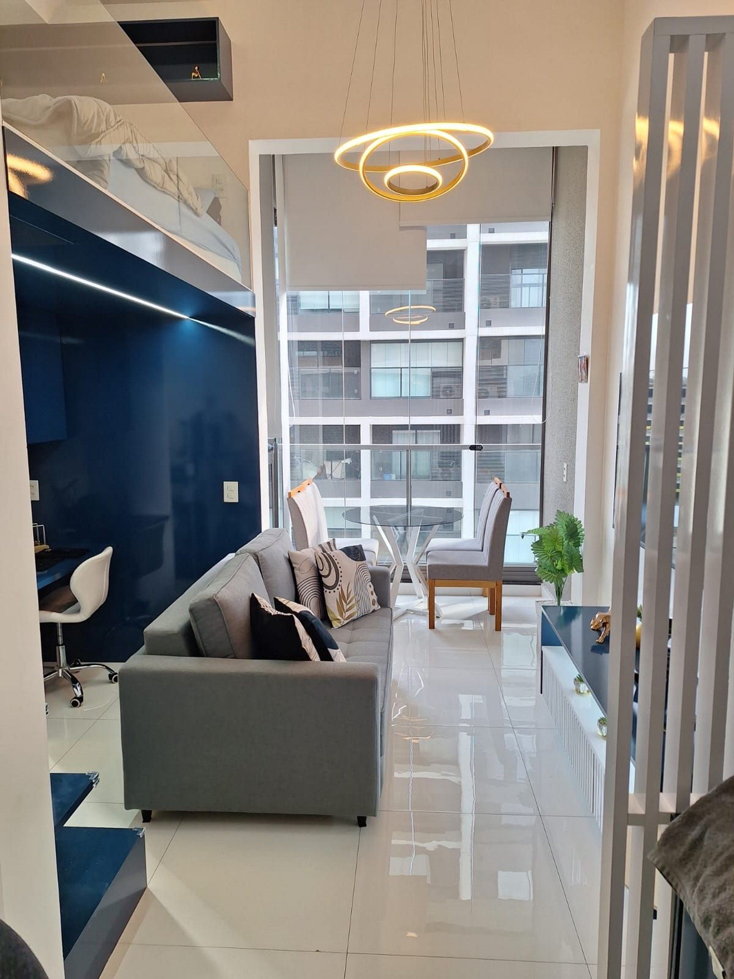 A modern living room with a grey sofa, a glass coffee table, and a view of a building through large windows.