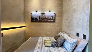 A compact hotel room with a bed, a wall-mounted picture, and a light strip along the wall.