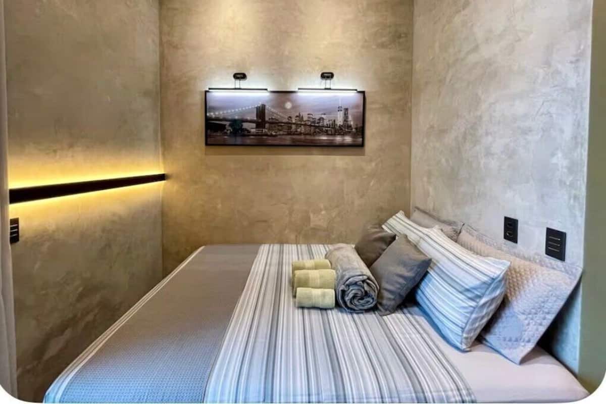 Une chambre d’hôtel de taille réduite, comprenant un lit, un tableau accroché au mur et une bande lumineuse le long du mur.
